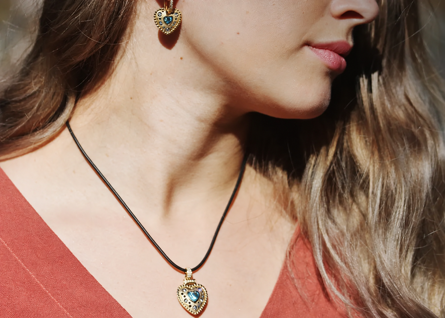 Blue topaz heart pendant and matching gold earrings worn with a warm coral blouse